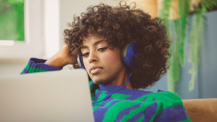 Stock image of a woman wearing headphones sitting on a sofa and focused on her laptop